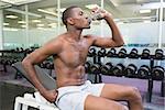 Side view of a young shirtless man drinking water at the gym