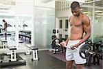 Determined young shirtless man lifting barbell in gym