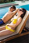 Side view of a young couple resting on sun loungers by swimming pool