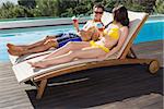 Romantic young couple with drinks sitting by swimming pool