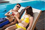 Smiling young couple toasting drinks by swimming pool