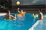 Cheerful young people playing with ball in swimming pool