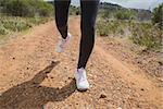 Low section of fit young woman running on country road