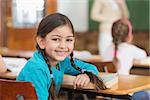 Cute pupil smiling at camera at her desk in classroom at the elementary school