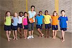 Cute pupils smiling at camera with PE teacher at the elementary school