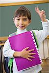 Cute pupil smiling at camera in classroom holding notepad at the elementary school