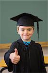 Cute pupil in mortar board smiling at camera in classroom at the elementary school