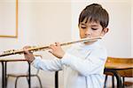 Cute pupil playing flute in classroom at the elementary school