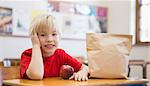 Cute pupil smiling at camera at desk in classroom at the elementary school