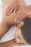 Beautiful brunette lying on massage table with salt scrub on back at the health spa