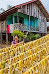 Nong Khiaw, Luang Prabang Province. A smiling woman hangs grapefruit peel out to dry in front of her house.  The peel will be made into a mosquito repellent.
