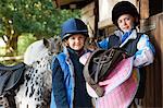 Two girls holding saddles with pony