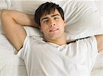 Young man lying on bed with hands behind head, portrait