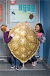 Two girls standing behind green sea turtle shell