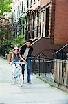 Daughter learning to ride bicycle along sidewalk with mother