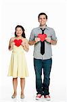 Young couple holding heart shapes against white background