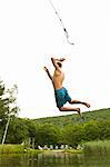 Teenage boy swinging off a rope into a lake