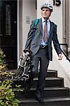Mid adult businessman carrying folding bicycle down steps