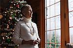 Mature woman standing by Christmas tree, looking through window