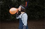 Young woman in headdress, blowing up a balloon