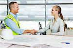 Engineer shaking hands with architect at desk of blueprints in office