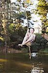 Young girl using rope swing over lake