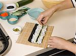 Woman preparing sushi roll at table