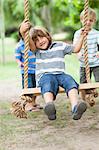 Boys pushing friend on tree swing