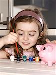 Smiling girl painting piggy bank