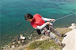 Woman climbing rocky coastal cliff