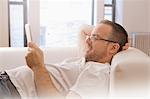 Mature man reclining on sofa looking at digital tablet