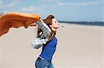 Young woman holding up blanket on windy beach