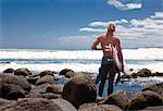 Young adult male surfer watching sea from beach rocks