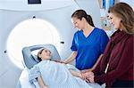 Radiographer and mother reassuring girl going into CT scanner