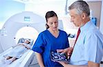 Girl in CT scanner, doctor and radiographer looking at scan on digital tablet