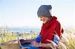 Young woman using laptop whilst sitting on hilltop