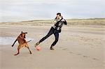 Mid adult man with dog playing football on beach, Bloemendaal aan Zee, Netherlands