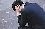 Desperate Japanese young businessman in a suit sitting on a bench in a park