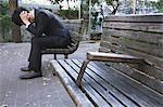 Desperate Japanese young businessman in a suit sitting on a bench in a park