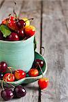 Ripe sweet mixed cherry in teal cup with saucer on old wooden table. Selective focus.