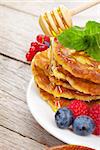 Pancakes with raspberry, blueberry, mint and honey syrup. On wooden table with copy space