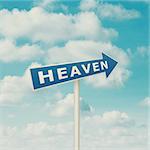 Road sign pointing to heaven, blue sky with clouds as background in vintage retro style.