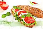 Wholegrain baguette with fresh mozzarella, tomatoes, lettuce and basil on kitchen towel.