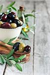 Mixed marinated olives (green, black and purple) in ceramic bowl and wooden spoon with bottle of olive oil. Selective focus. Copy space background