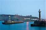 Two breakwater navigation beacons on the ends of the piers on either side of the entrance to Whitby harbour at dusk with St Marys Chrch and Whitbey Abbey visible on Tate Hill in the distance