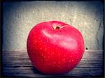 Ripe red apple on old wooden table against concrete wall.