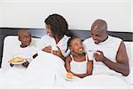 Family relaxing together in bed having breakfast at home in the bedroom