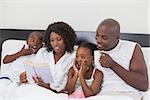 Family relaxing together in bed reading book at home in the bedroom