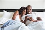 Happy couple cuddling in bed with smartphone at home in the bedroom