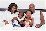 Happy family playing video games together in bed at home in the bedroom
